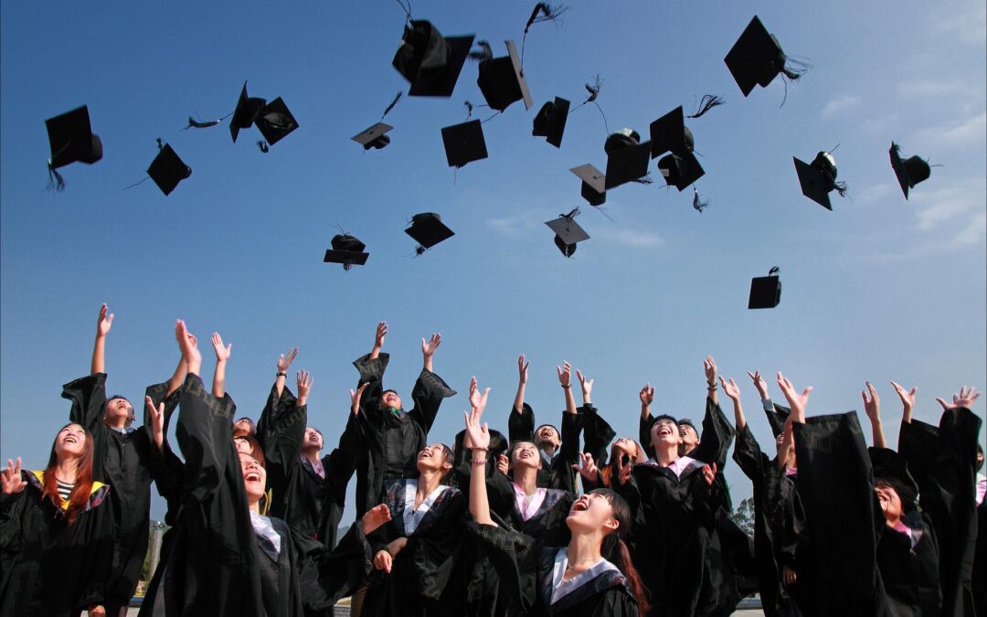 newly graduated people wearing black academy gowns throwing hats up in the air
