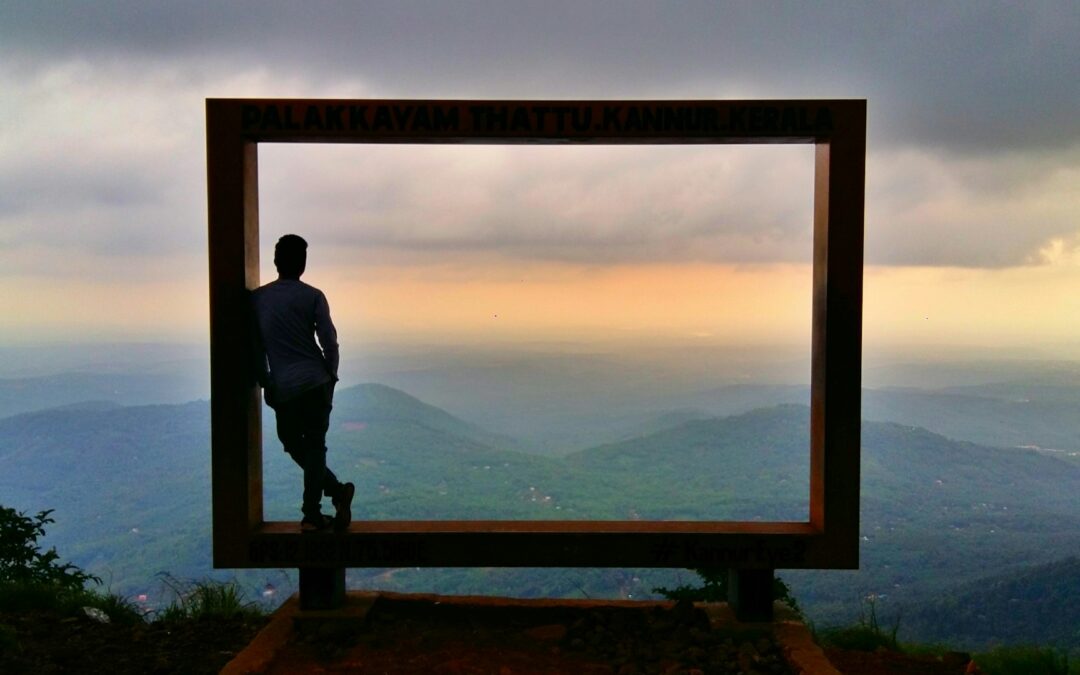 Hombre en chaqueta negra de pie en la cerca de madera marrón mirando las montañas durante el día